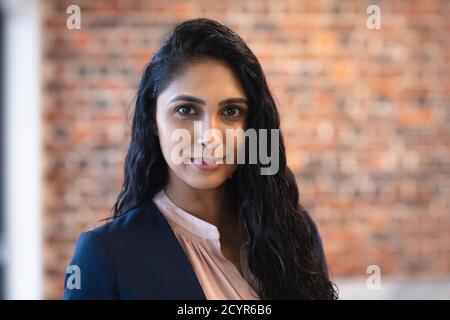 Ritratto di una donna di razza mista che lavora in un ufficio casual, guardando la macchina fotografica. Distanza sociale sul posto di lavoro durante la pandemia di Coronavirus Covid 19. Foto Stock