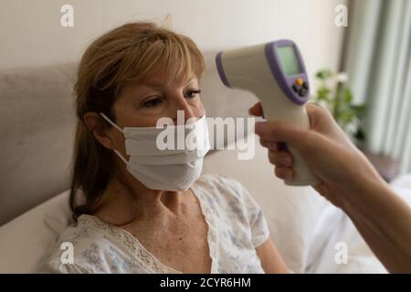 Donna caucasica anziana a casa visitata da infermiere caucasica, controllo della temperatura. Assistenza medica a casa durante la quarantena di Coronavirus Covid 19. Foto Stock