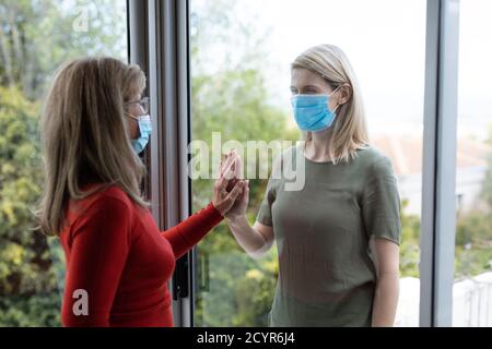 Donna caucasica anziana e sua figlia adulta a casa, indossando maschere per il viso e salutarsi a vicenda toccando le mani. Distanza sociale, salute e hyg Foto Stock