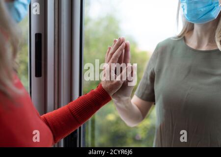 Donna caucasica anziana e sua figlia adulta a casa, indossando maschere per il viso e salutarsi a vicenda toccando le mani. Distanza sociale, salute e hyg Foto Stock