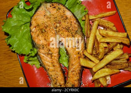 Trota alla griglia con patatine fritte . Piatto da pranzo rosso Foto Stock