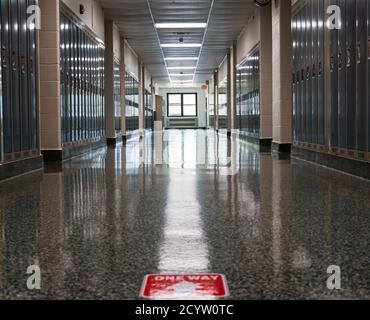Un corridoio vuoto della scuola superiore con un cartello a senso unico sul pavimento come parte della normale starnuto per aprire le scuole in una pandemia. Foto Stock