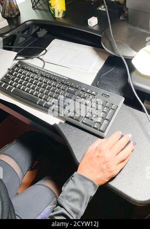 Vista posteriore delle donne che lavorano da casa alla sua scrivania con la tastiera del computer e la mano sul mouse. Foto Stock