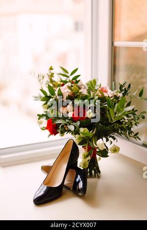 Scarpe nere su un davanzale bianco con bouquet nuziale alla finestra aperta. Foto Stock