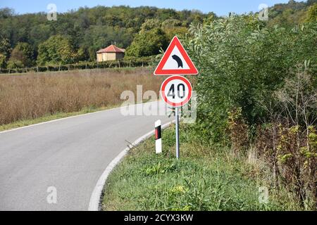 Segnaletica stradale che indica la velocità massima di 40 chilometri per ora e signa che avverte i piloti su curve strette la strada che ci attende Foto Stock