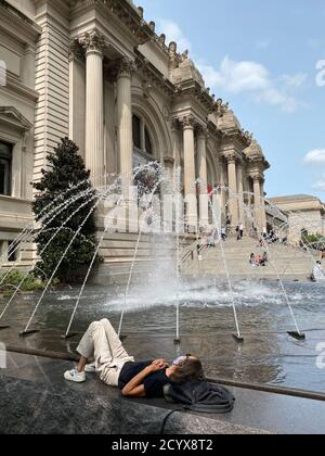 La donna si rilassa guardando lo spettacolo d'acqua della fontana di fronte Il Metropolitan Museum of Art sulla 5th Avenue a New Città di York Foto Stock