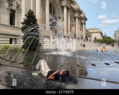 La donna si rilassa guardando lo spettacolo d'acqua della fontana di fronte Il Metropolitan Museum of Art sulla 5th Avenue a New Città di York Foto Stock