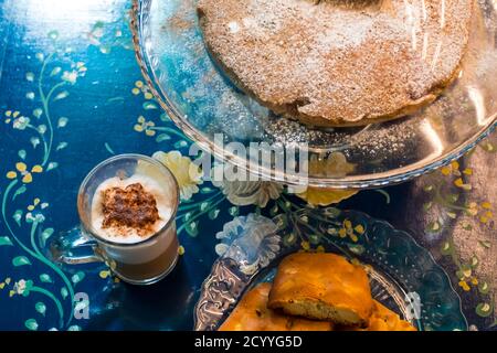 La gustosa torta alla cannella fatta in casa con zucchero, accompagnata da una tazza di caffè fresco con cioccolato e alcuni gustosi e sani biscotti alle mandorle, ricchi di vi Foto Stock