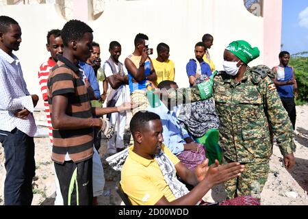 Una donna ugandese che opera sotto la missione dell'Unione Africana in Somalia (AMISOM) aiuta i membri di una comunità locale somala a disinfettare le mani mentre dimostra come usare i disinfettanti per le mani. AMISOM ha consegnato gli oggetti donati dal Governo italiano in collaborazione CON LA CARITAS, alla comunità locale del distretto di Wadajir, nei pressi del campo base AMISOM, per contribuire a prevenire la diffusione del virus il 12 giugno 2020. Foto Stock