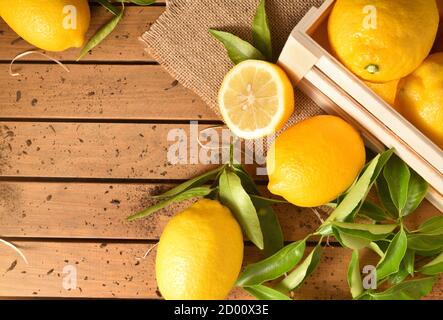 Cassa di fondo di limoni di limoni agricoli biologici appena raccolti con rami pieni di foglie su una tavola di legno con terreno. Vista dall'alto. COM. Orizzontale Foto Stock