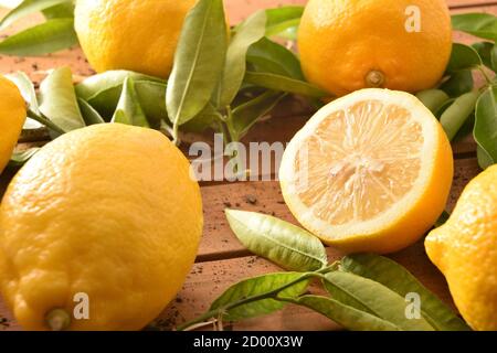 Limoni agricoli biologici appena raccolti con rami pieni di foglie su una base di legno con terreno. Vista rialzata. Composizione orizzontale. Foto Stock