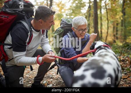 Coppia anziana trekking con il cane nel bosco; stile di vita in pensione attivo Foto Stock