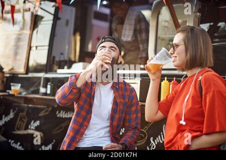 Una coppia di hipster che si rilassa con la birra davanti al cibo carrello Foto Stock