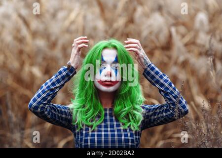 Ritratto di una ragazza con capelli verdi con trucco joker su un arancio foglie di sfondo canne. Foto Stock