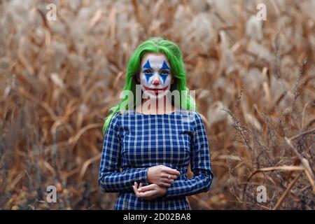 Ritratto di una ragazza con capelli verdi con trucco joker su un arancio foglie di sfondo canne. Foto Stock