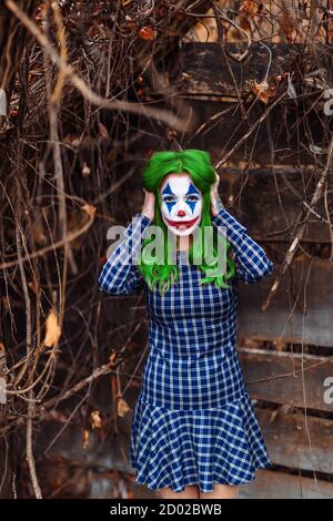 Ritratto di una ragazza con capelli verdi in abito da masticare con trucco joker su sfondo di legno atmosferico. Foto Stock