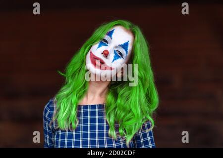 Primo piano ritratto di una ragazza dai capelli verdi in abito da masticare con trucco joker su uno sfondo marrone sfocato. Foto Stock