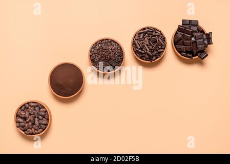 Fagioli di cacao organici e pezzi di cioccolato in ciotole di ceramica, isolati su sfondo beige. Piatto con ingredienti di cioccolato e cacao in polvere. Foto Stock