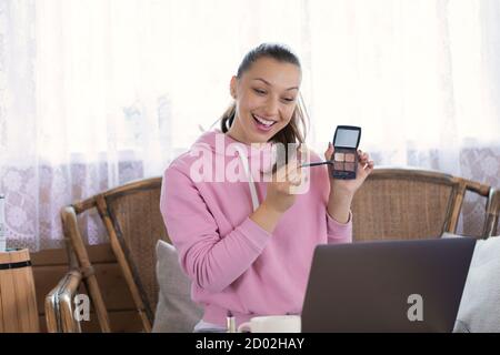 Giovane blogger di bellezza sorridente con eyeshadows record vlog su laptop a casa Foto Stock