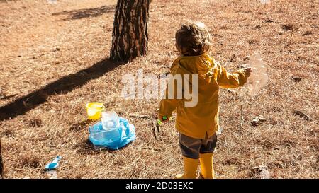Il bambino giovane sta raccogliendo i rifiuti di plastica nella foresta come volontario. Concetto di educazione ambientale precoce per bambini e bambini piccoli. Senza plastica Foto Stock