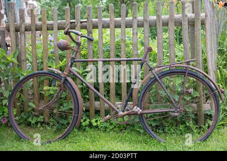 Vecchia bicicletta arrugginita appoggiata a una recinzione di legno Foto Stock