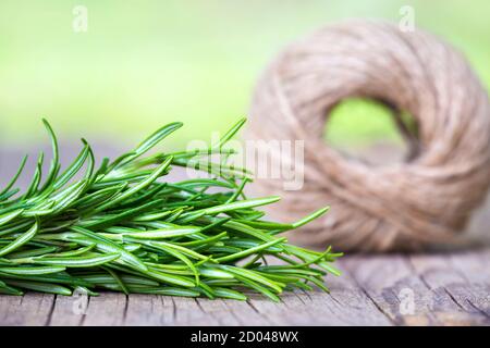 Rosmarino verde fresco di erbe e rotolo di spago di iuta su un tavolo in legno con spazio per la copia Foto Stock