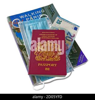 Un passaporto britannico con banconote in euro, una guida a Parigi e una maschera, in risposta al viaggio con la pandemia del Covid-19 nel 2020 Foto Stock