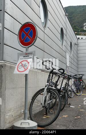 Biciclette parcheggiate lungo un muro di un edificio. Le biciclette sono collocate sotto il cartello di divieto di parcheggio. Il cartello dice in italiano: Parcheggio vietato. Foto Stock