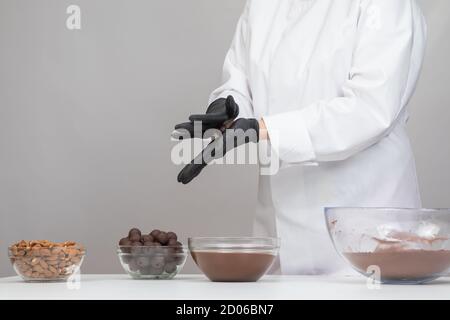 Cioccolatiere in uniforme, passo dopo passo, per la produzione di tartufi di cioccolato fondente artigianali Foto Stock