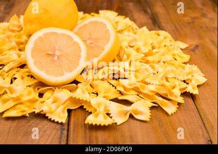 Pasta secca farfalle e limoni su sfondo ligneo. Pasta colorata, cucina tipica italiana del sud. Foto di alta qualità. Spazio di copia Foto Stock