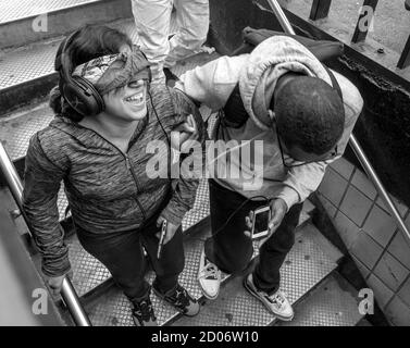 Un giovane conduce una giovane donna, bendata , lungo i gradini della metropolitana. Foto di Liz Roll Foto Stock