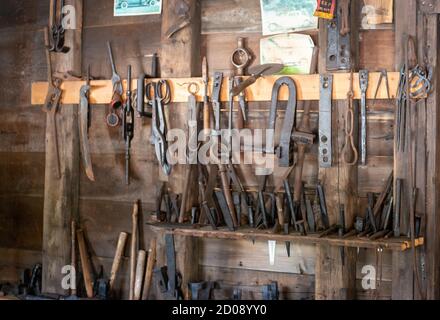 Una collezione di utensili di fabbro vintage appesi su scaffali su un muro di legno in un granaio di pietra. Foto Stock