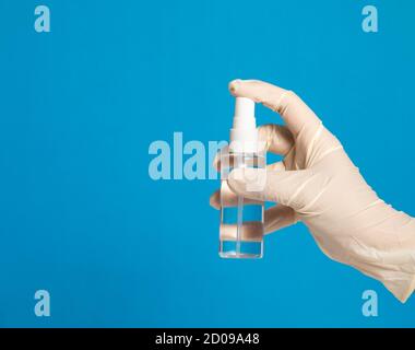 la mano che indossa un guanto di plastica ha spruzzato un disinfettante sopra a. sfondo blu Foto Stock