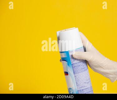 la mano che indossa un guanto di plastica ha spruzzato un disinfettante sopra a. sfondo giallo Foto Stock