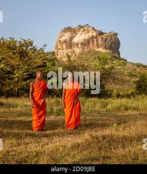 Negombo, Sri Lanka - 2019-03-22 - i monaci a piedi nel campo di erba con Roccia di Sigiriya in background. Foto Stock