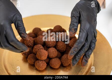 Lo chef del closeup mette in oro una pila di tartufi al cioccolato fondente polvere sulla piastra dorata Foto Stock