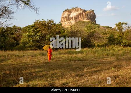 Negombo, Sri Lanka - 2019-03-22 - i monaci a piedi nel campo di erba con Roccia di Sigiriya in background. Foto Stock