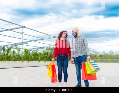 coppia di un uomo e una donna che indossa maschera di faccia tenendo le mani dopo lo shopping sulle vendite per il venerdì nero. concetto circa consumismo e divertimento per acquistare Foto Stock