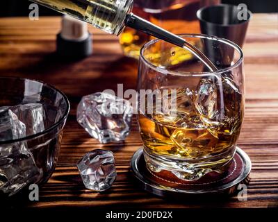 Versare il whisky in un bicchiere con cubetti di ghiaccio - whisky sulle rocce Foto Stock