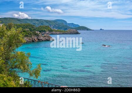 Bellissimo paesaggio con baia di mare con acqua turchese, rocce e scogliere coperte di alberi verdi e cespugli, cielo blu e nuvole bianche. Isola di Corfù, Foto Stock