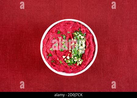 Hummus di barbabietola fatto in casa in ciotola su sfondo rosso. Vista dall'alto, disposizione piatta Foto Stock