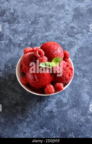 Sorbetto al lampone, paletta per gelato con bacche fresche in recipiente su sfondo di pietra blu con spazio libero per il testo. Gustoso dessert estivo freddo Foto Stock