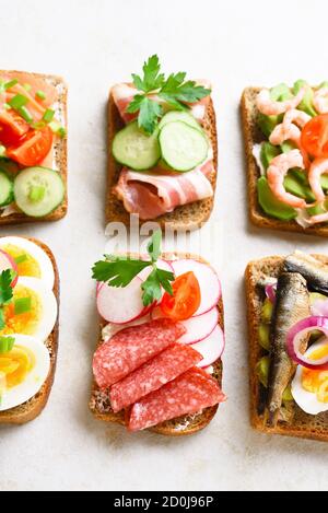 Primo piano di diversi panini con carne, verdure e pesce. Assortimento di panini aperti su sfondo in pietra chiaro. Gustoso snack sano. Foto Stock