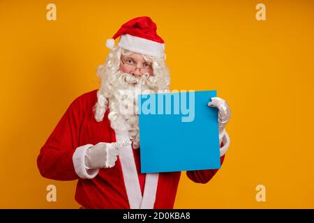 Attore maschile in un costume di Babbo Natale tiene in le sue mani un foglio blu di carta per i dischi e. posa su sfondo giallo Foto Stock