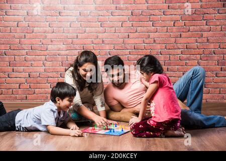 Giovane famiglia indiana di quattro giochi da tavolo come Scacchi, Ludo o snack e ladder a casa in quarantena Foto Stock