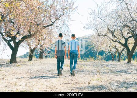 Bambini che camminano in giardino fiorito di mandorle in giornata di sole In Spagna Foto Stock