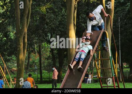 Dhaka, Bangladesh. 03 ottobre 2020. Un bambino che indossa un facemask visto giocare con suo padre al parco di Ramna durante la pandemia di Coronavirus. Dopo un periodo di sei mesi a causa della pandemia di coronavirus, Ramna Park ha riaperto per il pubblico. Credit: SOPA Images Limited/Alamy Live News Foto Stock