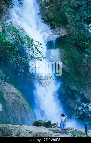 Vista posteriore della donna europea si erge su pietra calcarea e scatta foto con la fotocamera digitale di fronte alle cascate Kuang si. Luang Prabang, Laos. Foto Stock