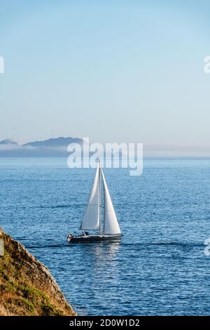 Una barca solitaria si allontana dalla Ria de Pontevedra in Galizia al tramonto, con le Isole Cies sullo sfondo. Foto Stock