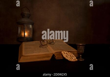 una vita morta di una bibbia con un vecchio peltro lampada con una luce del tè che brucia con una vecchia bibbia e cena Foto Stock